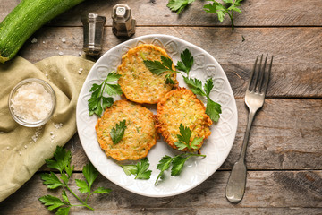 Plate with zucchini pancakes on wooden table