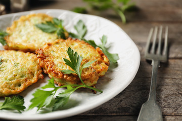 Plate with zucchini pancakes on wooden table