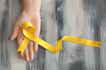 Woman holding yellow ribbon on wooden background. Cancer awareness concept
