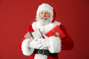 Santa Claus with gift boxes on color background