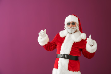 Fototapeta na wymiar Cool Santa Claus showing thumb-up on color background