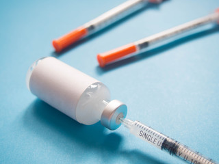 Close up of blank label medical glass vial with plastic single-use syringes on blue background. Concept of immunization, insulin hormone, vaccination, cosmetic injection and health care.