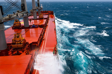Cargo ship rolling in stormy sea. Huge waves under blue sky in Indian Ocean