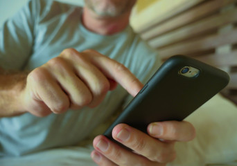 close up hands holding mobile phone of young man at home bedroom using internet social media app on smartphone networking and texting from bed