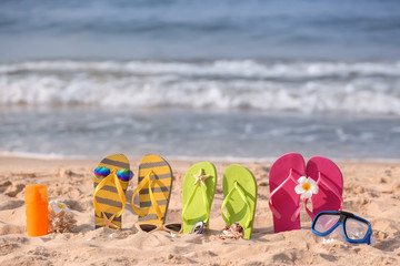 Set of flip-flops with beach items on sand near sea