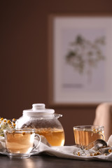 Glass cups and teapot of delicious chamomile drink on table