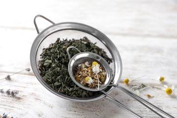 Sieves with dried chamomile and tea leaves on white wooden table