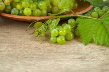 Ripe grape cluster of white grapes on a wooden table with green grape leaves. The harvest of grape...
