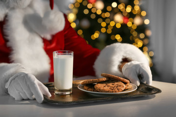 Santa Claus eating cookies and drinking milk at table, closeup