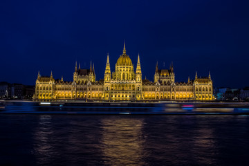 Fototapeta premium long exposure photography beautiful concept of Budapest parliament buildings architecture symmetry facade on riverfront shore with fuzzy illuminated cruise ship