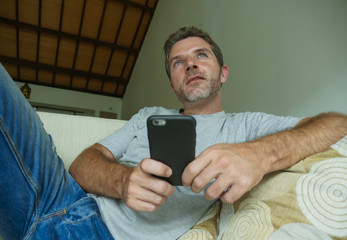 lifestyle indoors portrait of young happy and attractive man at home sofa couch using internet social media app on mobile phone networking relaxed