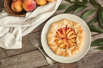 Plate with delicious peach galette on wooden table