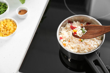 Spoon with boiled rice and vegetables over saucepan on stove