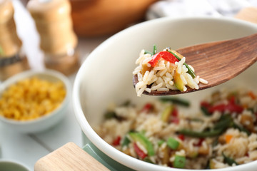 Spoon with boiled rice and vegetables over saucepan, closeup