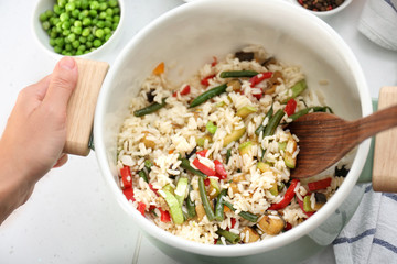 Woman cooking tasty rice with vegetables in saucepan