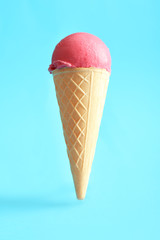 Waffle cone with delicious strawberry ice-cream on color background