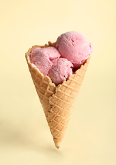 Waffle cone with delicious strawberry ice-cream on color background