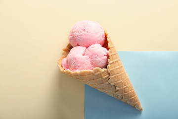 Waffle cone with delicious strawberry ice-cream on color background