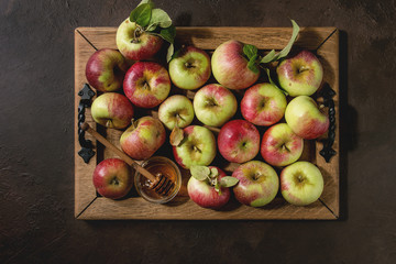 Ripe organic gardening green red apples with leaves and jar of honey on wooden tray over dark texture background. Flat lay, space. Autumn harvest.
