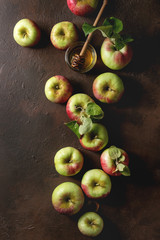 Ripe organic gardening green red apples with leaves and jar of honey over dark texture background. Flat lay, space. Autumn harvest