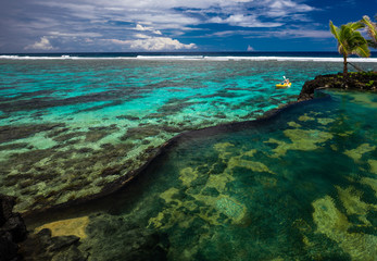 Female and little boy paddling canoe on a lagoon with coral reef.