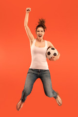 Forward to the victory.The young woman as soccer football player jumping and kicking the ball at studio on a red background. Football fan and world championship concept. Human emotions concepts