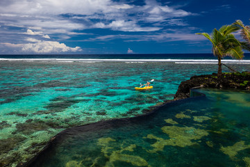 Female and little boy paddling canoe on a lagoon with coral reef.