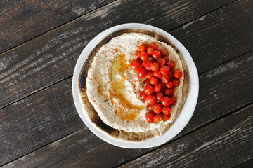 Top view chickpea hummus served on flatbread with cherry tomatoes on wooden table