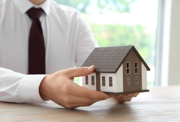 Real estate agent with house model at wooden table. Mortgage concept