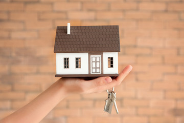 Woman holding house model and key against brick wall. Mortgage concept