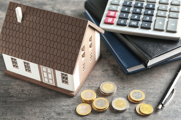 House model, calculator and coins on grey table. Mortgage concept
