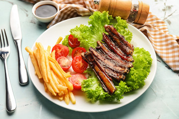 Delicious grilled ribs with french fries and vegetables on plate