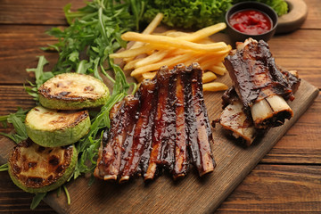 Delicious grilled ribs with french fries, arugula and zucchini on wooden board