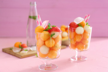 Glasses with tasty melon balls on color table