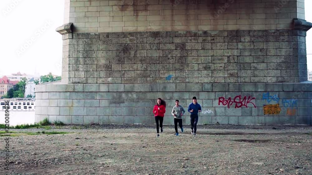 Wall mural Young athlete friends running under the bridge in the city.