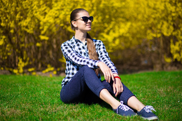 Young girl relax in park on fresh green grass near tree in yellow blossom. Summer time