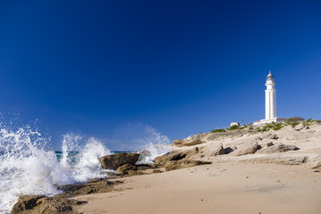Fototapeta premium lighthouse on trafalgar beach with waves breaking on rocks in a sunny day with blue sky