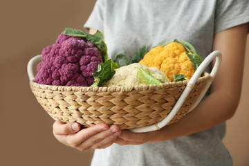 Woman holding wicker basket with colorful cauliflowers, closeup