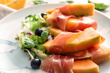 Delicious melon wrapped in prosciutto on plate, closeup