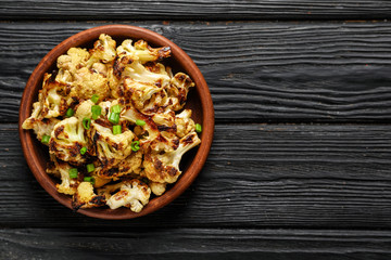 Plate with tasty grilled cauliflower and green onion on wooden table
