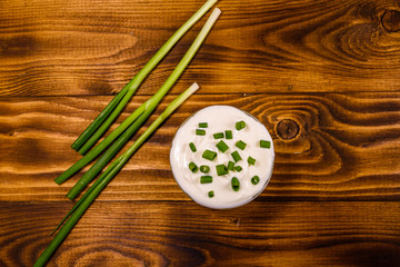 Glass bowl with sour cream and green onion on wooden table. Top view
