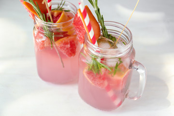Fresh grapefruit cocktail with rosemary in mason jars on light table