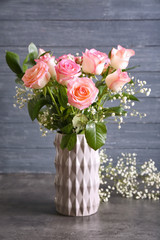 Vase with beautiful roses on grey table