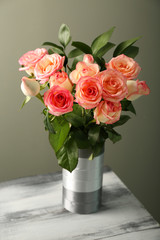 Vase with beautiful roses on wooden table against grey background