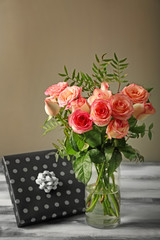 Vase with beautiful roses and gift box on wooden table