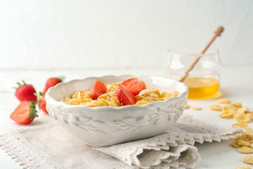 Bowl with healthy cornflakes and strawberry on white table