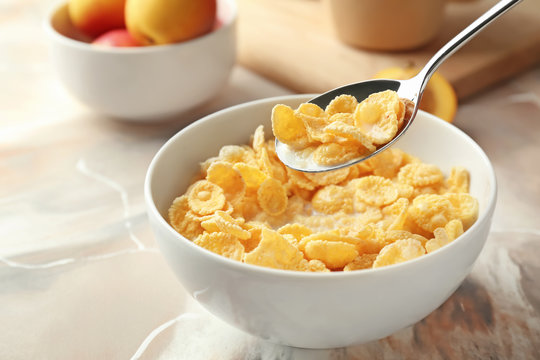 Eating of healthy cornflakes with milk from bowl on table, closeup