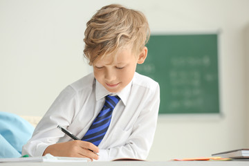 Cute little boy doing homework in classroom