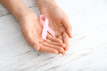 Woman holding pink ribbon on light wooden background. Breast cancer concept