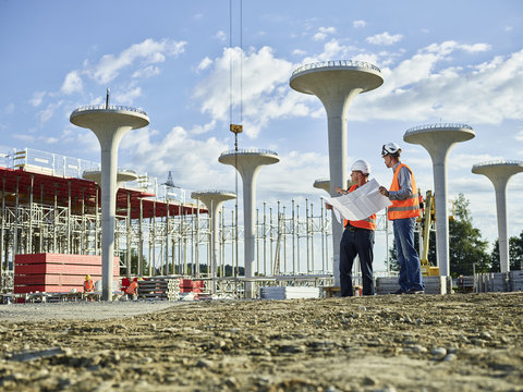 Workers on construction site looking at blueprint with the architect